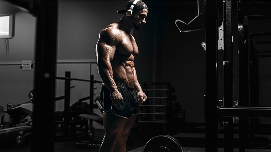 Muskul�s mand st�r med bar overkrop foran en v�gtstang.